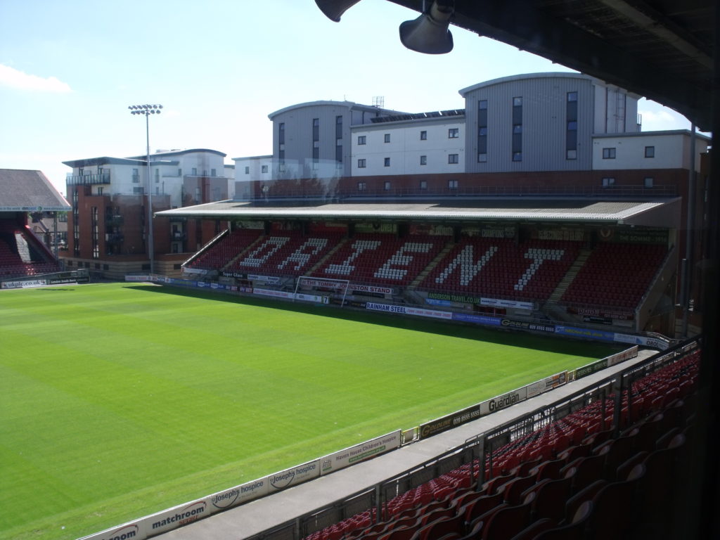 Ein Fußballfeld in der Sonne, dahinter eine Tribüne mit dem Schriftzug Orient